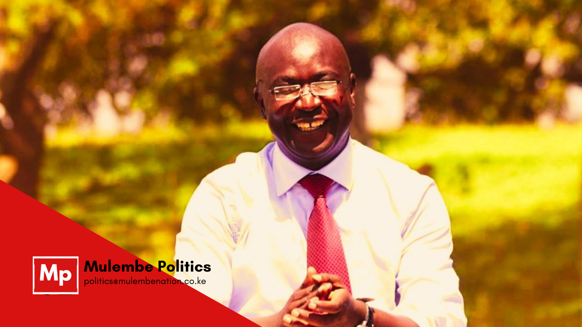 A smiling Wangamati in a shirt and tie and with his hands clasped together before him