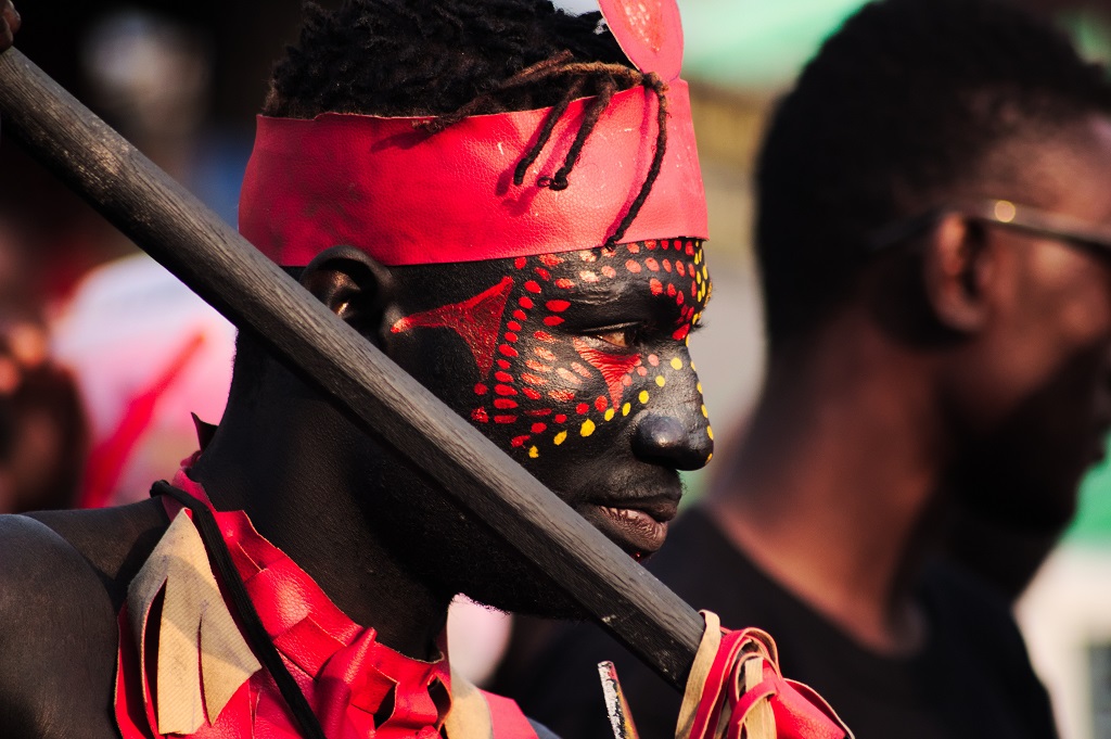 african warrior with red tribal marks on face and spear in hand in simillar fashion to the full warrior gear worn by the groom during customary Bukusu marriage