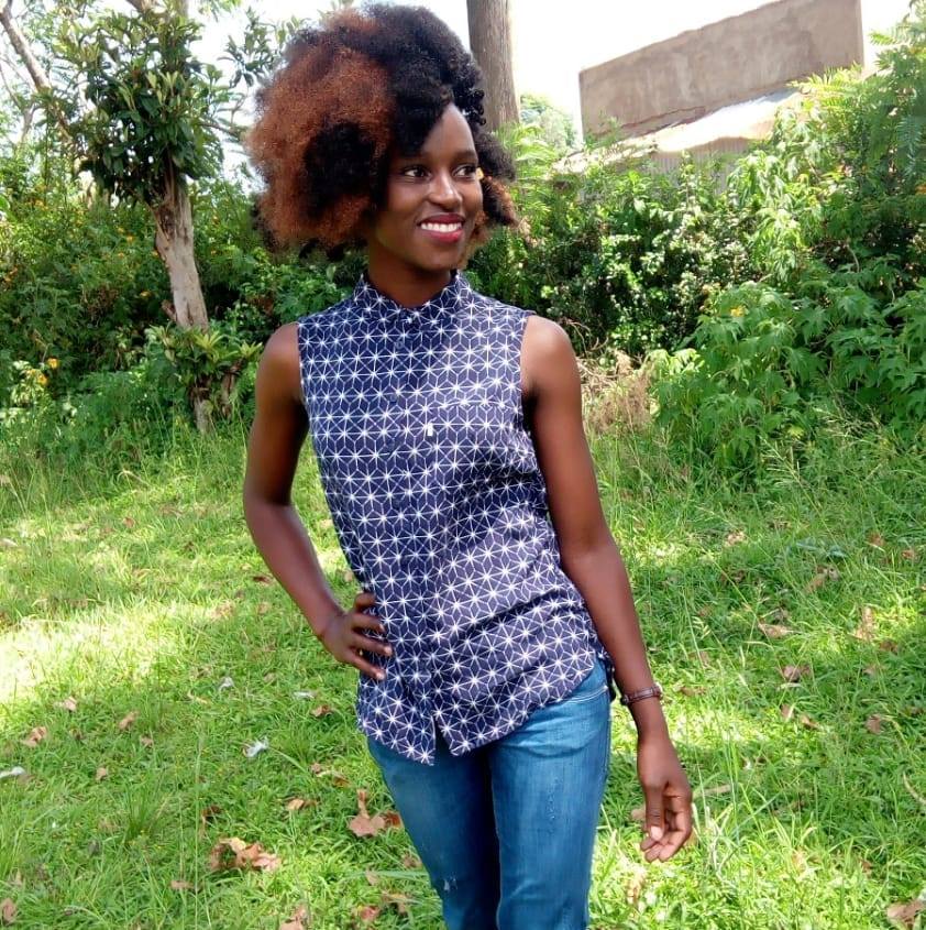 The Boss Lady of Luhya comedy Nakhumicha outdoors in a sleeveless top and blue jeans. 