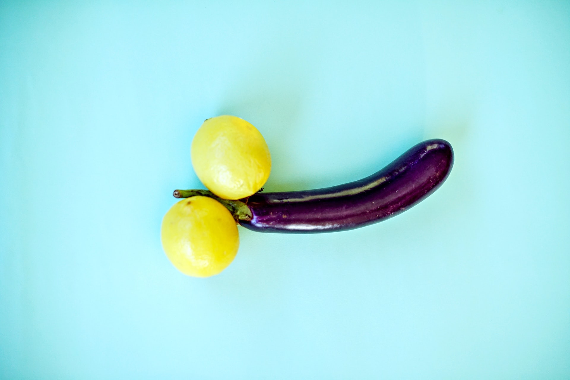 eggplant and two citrus arranged to simulate the male organs fruits upon a lilac background