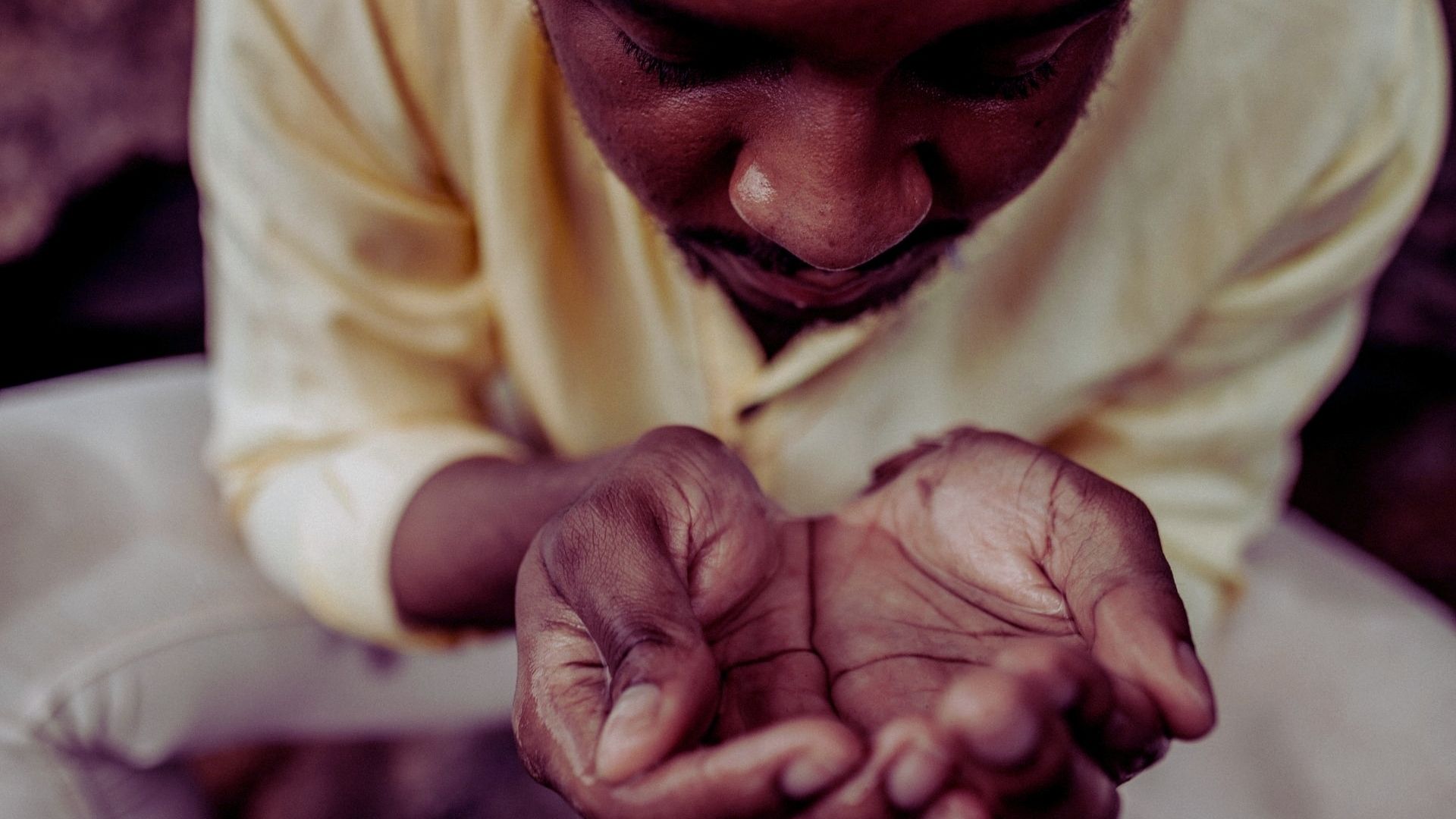man in yellow shirt crouched in begging position with hands cusped together